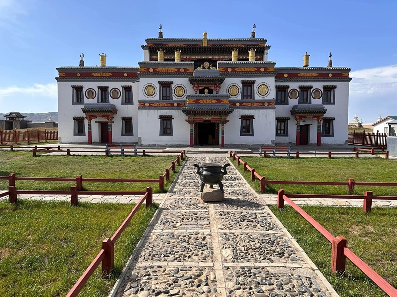 The white and gold facade of a temple at Erdene Zuu Monastery with a stone path and incense burner in the foreground.